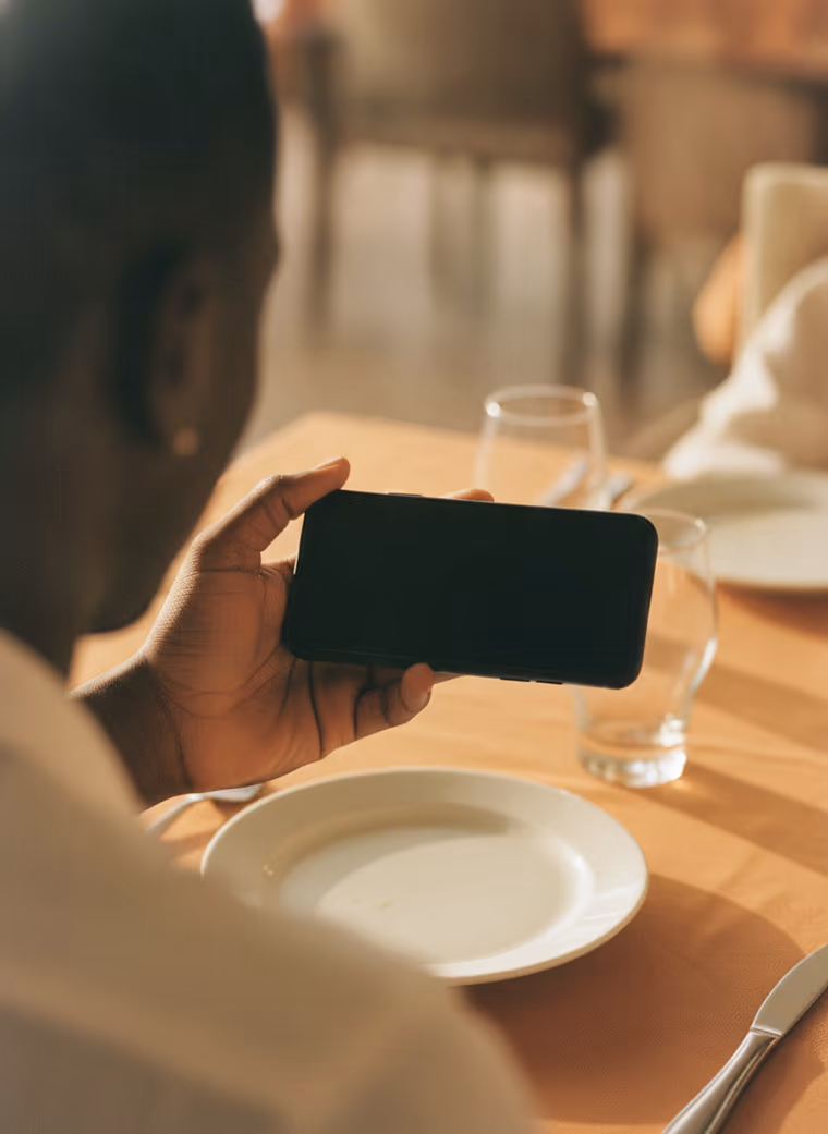 Une main tient un téléphone au-dessus d’une table de restaurant