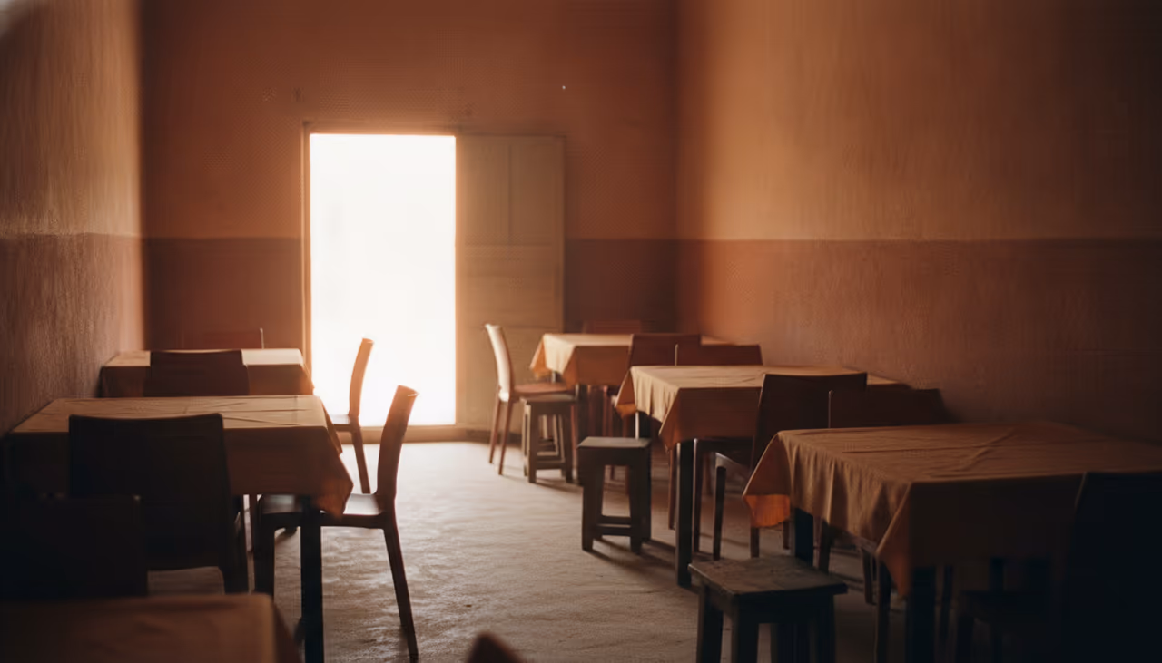 La salle d’un restaurant sénégalais en fin d’après-midi, tables nappées d’ocre, chaises vides